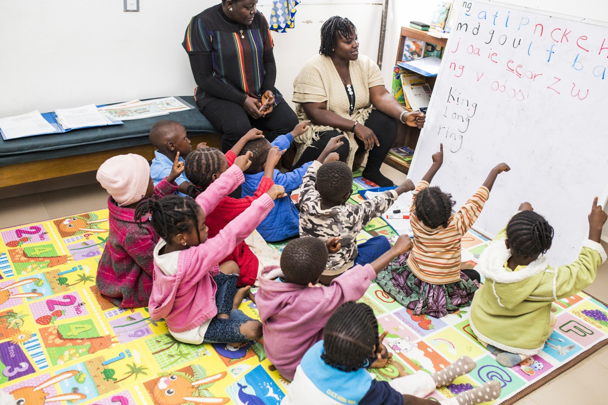 Children raising their hands during a lesson on a reading mat