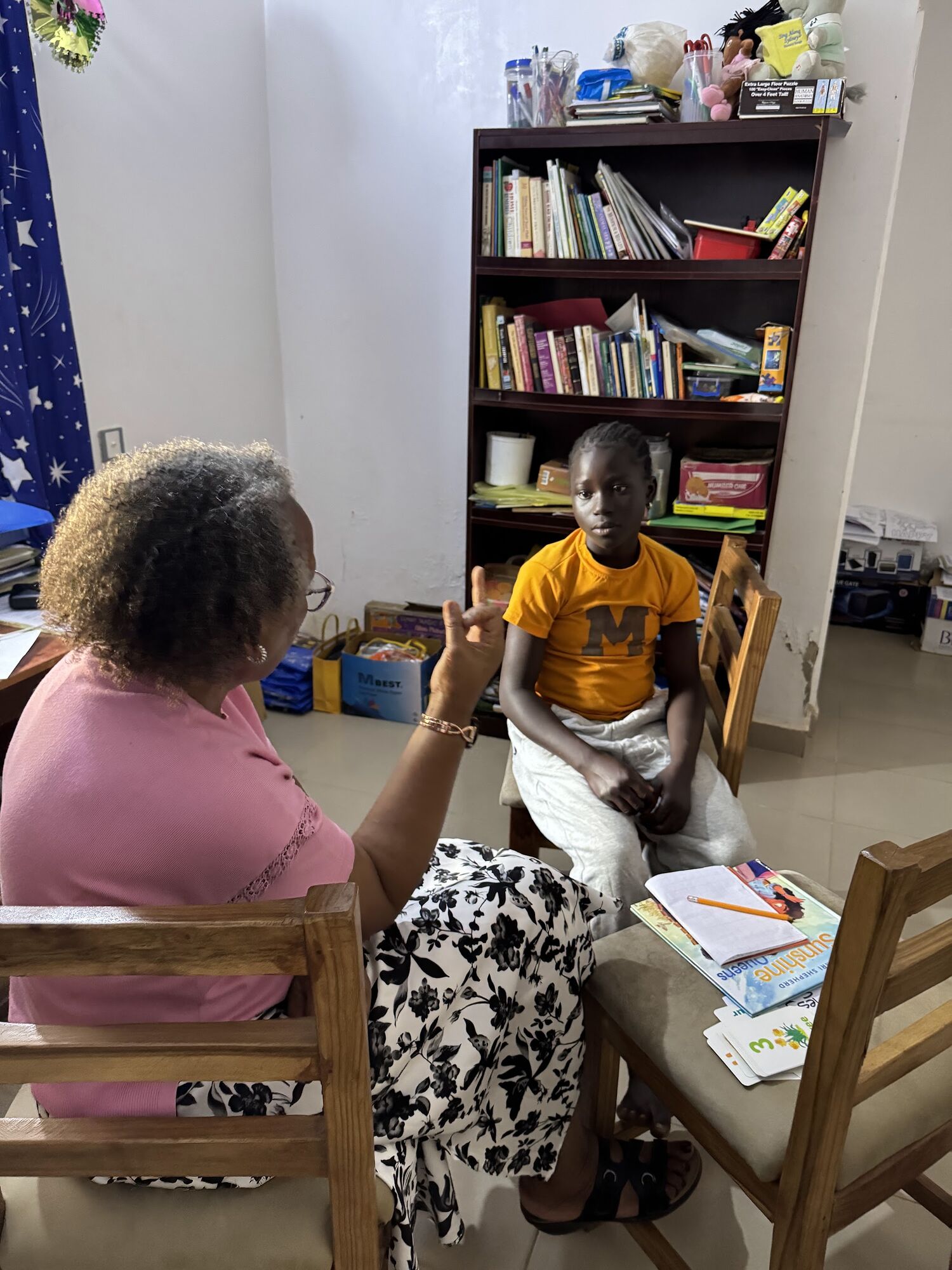 A learner reading with a volunteer beside a bookshelf